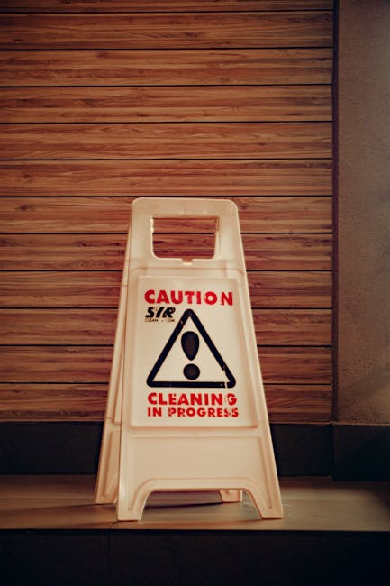 A person holding a sticker with a blue atom symbol, featuring a central dot and intersecting elliptical orbits, in front of a kitchen countertop with a wooden surface, stainless steel appliances, and