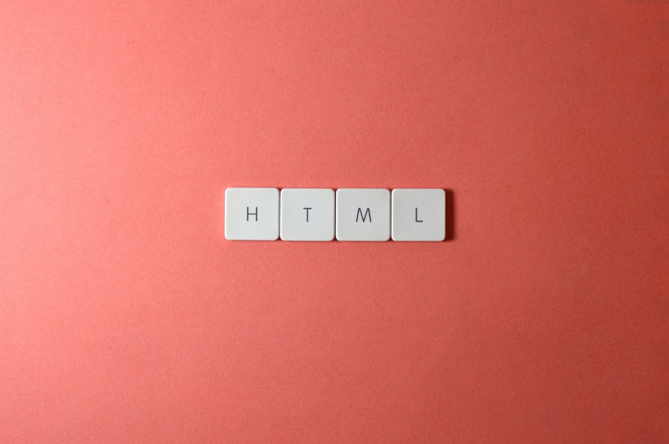 Close-up image of four white keyboard keys with black letters spelling HTML, arranged in a horizontal line on a pinkish coral background. The surface appears clean and smooth, with soft lighting highl